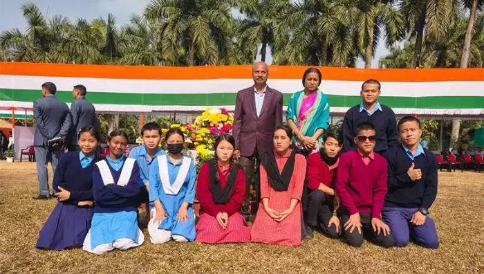 Students and teachers are seen gathered outdoors for a group photograph during a school celebration. The image reflects collective participation, unity, and pride among students and staff. The setting suggests a formal or commemorative school activity.