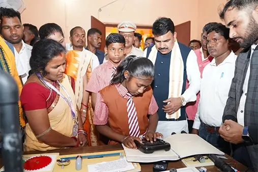 A student using the HEXIS Braille device with the Minister and other onlookers watching behind her.