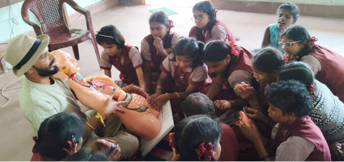 students of Rangarao Memorial School for Disabled, Mysuru, gather around a VE facilitator during an ARC on Wheels – Anubhav session. Using a tactile torso model, the children actively explore internal organs to understand the human body through touch and guided explanation.