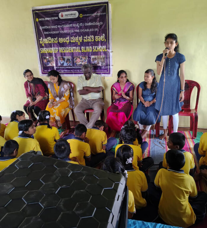 Students of Sneha Deepa Residential School for the Blind are seated in front of their teachers and VE facilitators, as one facilitator addresses the gathering during the ARC on Wheels session