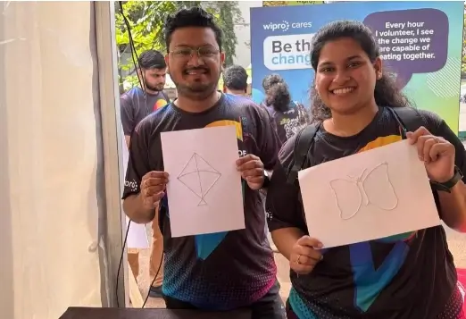 Wipro volunteers smile as they hold tactile creations made during the Spirit of Wipro Run. The cheerful image celebrates teamwork and inclusion in support of accessible education.